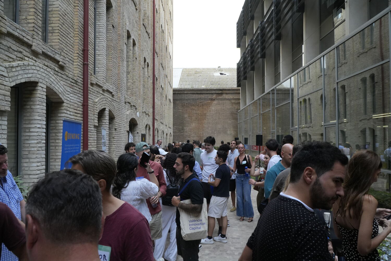 Attendees mingling in the brick courtyard of La Harinera during the Nomad Entrepreneur Fair, a València Innovation Capital tote bag in the foreground.