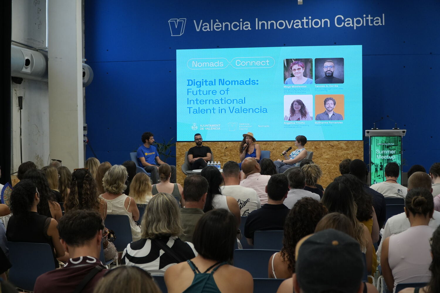 Maya Middlemiss moderating a four-person panel on stage in front of a seated audience, under a screen reading Digital Nomads: Future of International Talent in Valencia.