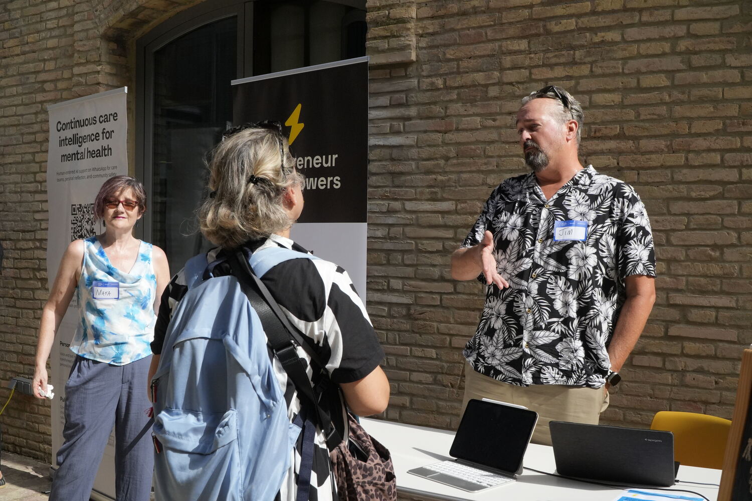 Jim Christian talking with two visitors at the Solopreneur Superpowers stand, laptops open on the table in front of a lightning-bolt banner.